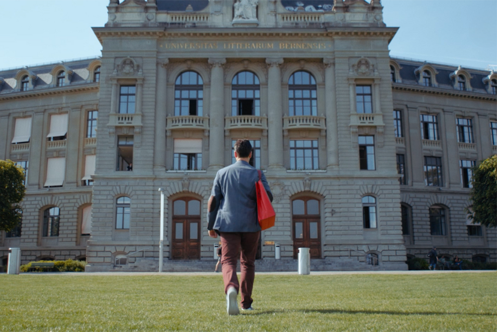 Man with continuing education bag in front of the main building of the University of Bern